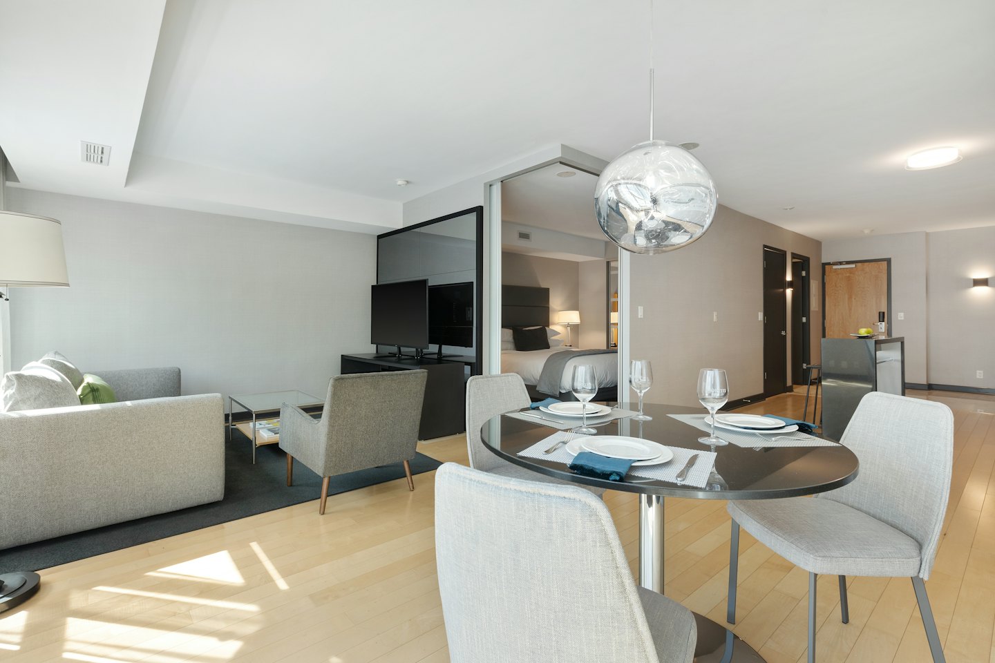 Sunlight illuminates a modern apartment with grey sofa and dining table.